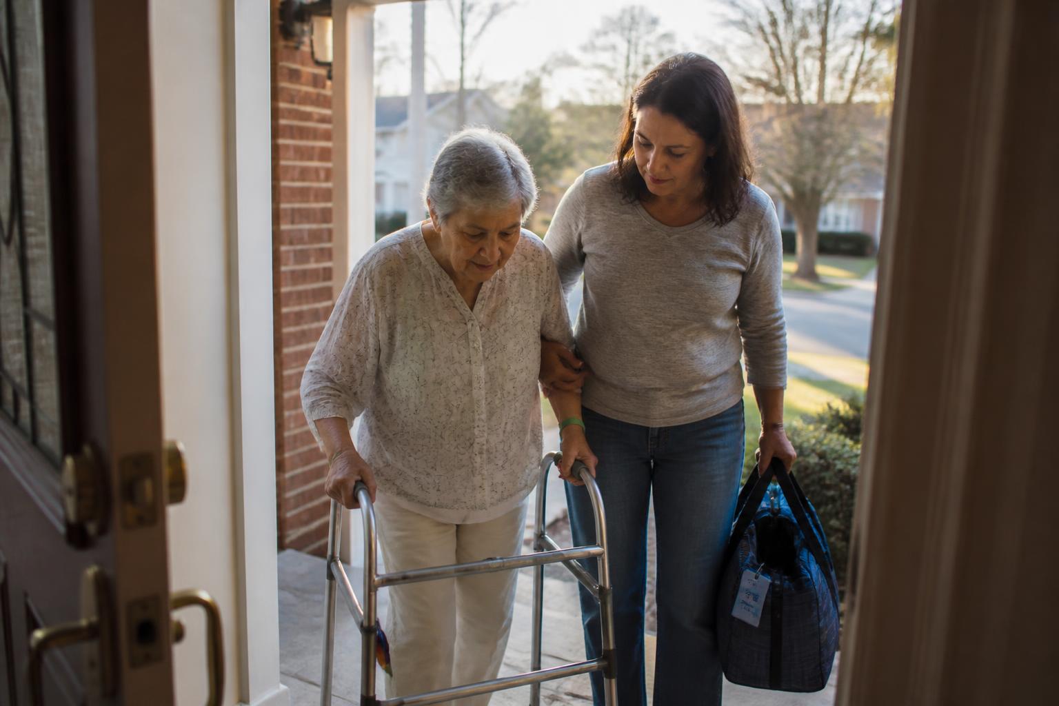An adult daughter helping her mother through the front door after a hospital stay